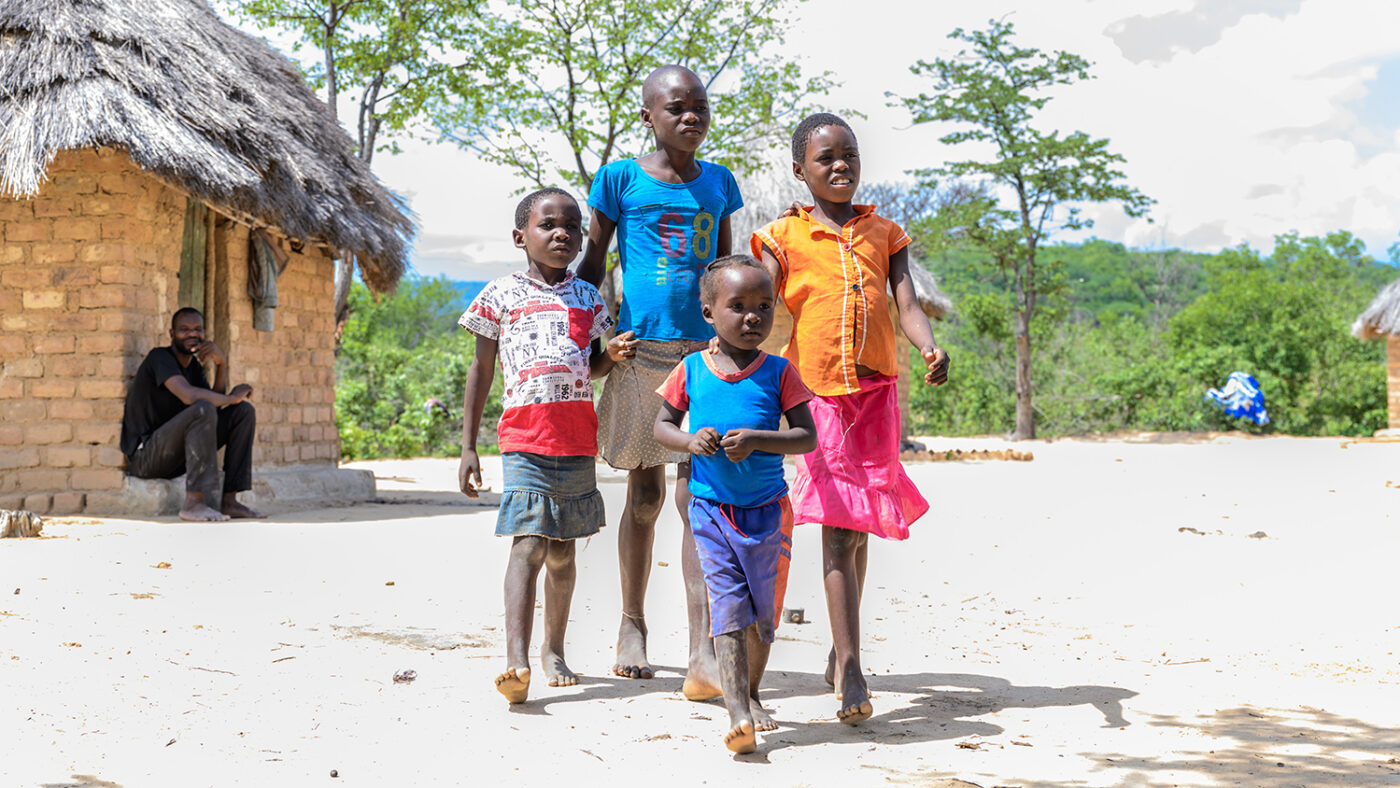 four children stand outside their home while their father looks on.