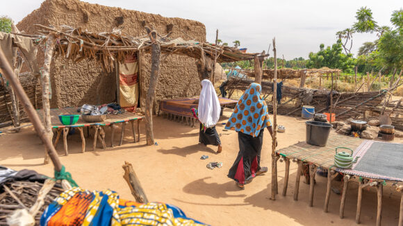 Two villagers in Niger walk among dusty coloured huts.