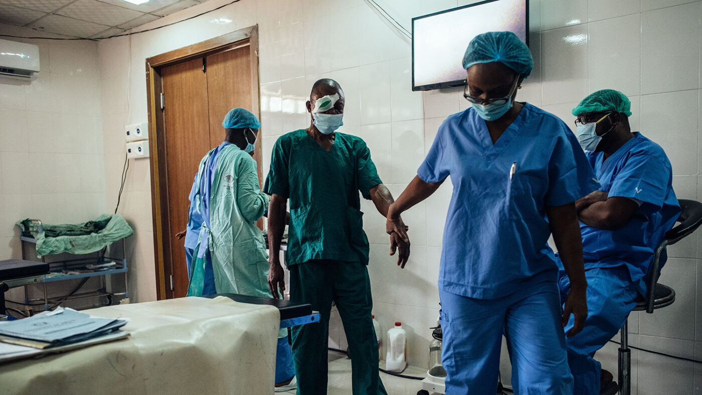 A nurse dressed in scrubs escorts a man out of the operating theatre after glaucoma surgery.