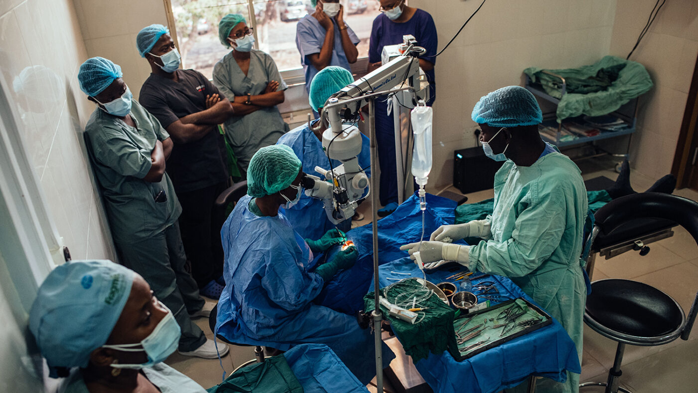 A surgeon performs eye surgery while a consultant and other trainees look on.