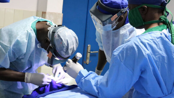 A group of surgeons wearing PPE perform eye surgery.