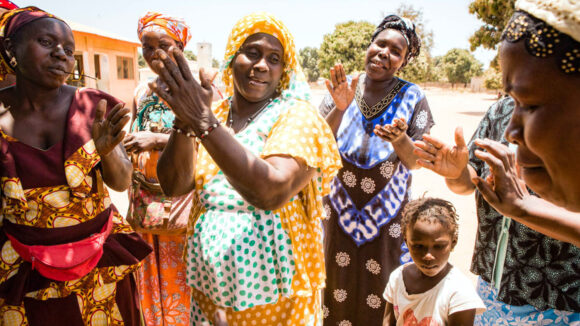 A group of women sing, dance, and clap their hands.