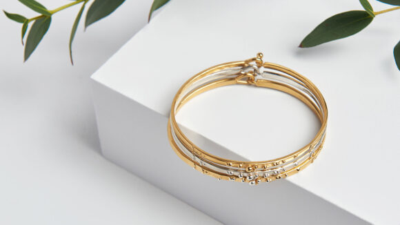 Three bracelets are stacked on top of each other. The design says 'love' in braille.