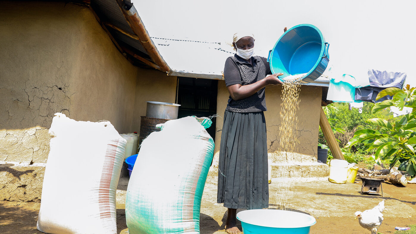 Hellen Odero pours grain from a bowl outside her home.
