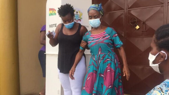 A woman wearing a mask helps another woman wearing a mask to walk down some steps.