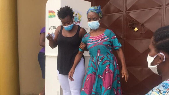 A woman assists another woman to walk down some steps. Both women are wearing face masks.