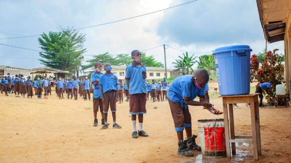 School children in Cameroon line up to wash their hands from a large bucket.