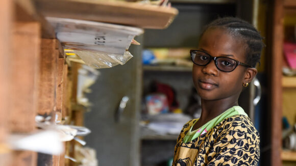 A young girl smiles as she stands in a classroom.