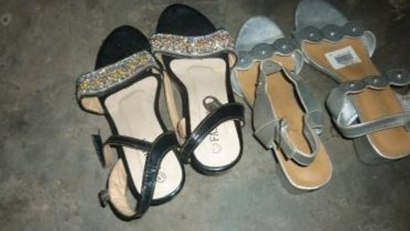Two pairs of open-toed women's shoes lie on a stone floor. One pair is black, while the other is grey.