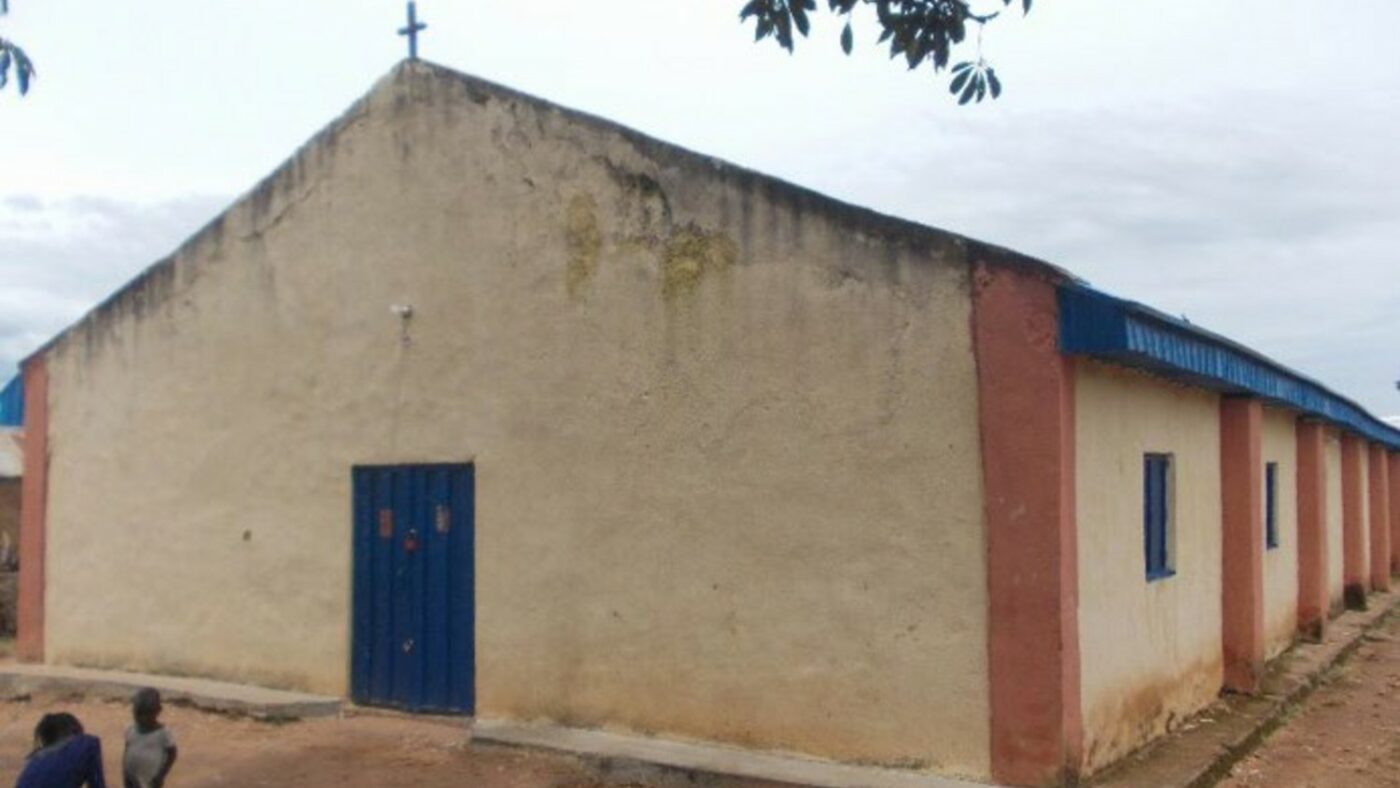 Pictured is a single-storey church building, with brown walls and blue doors and windows. On the church roof there is a small cross.