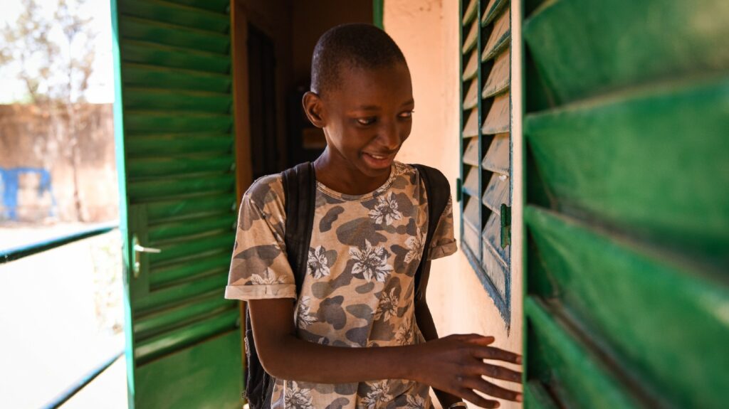 A young boy with a backpack walking through the corridor at school in Mali.