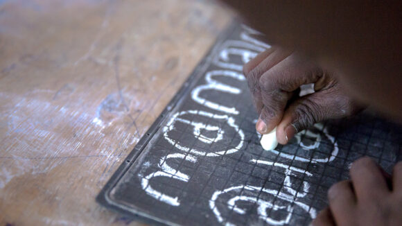 A boy using chalk to write on a slate.
