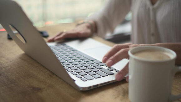 A close-up of a woman typing on a laptop, with a cup of tea next to her.