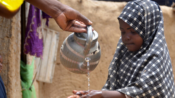 Young girl washing her hands with water poured from a teapot by her father.