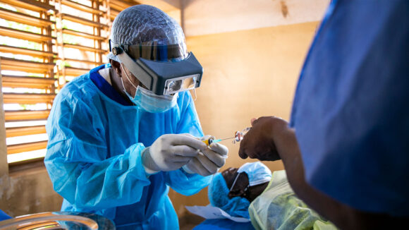 An eye surgeon wearing medical scrubs prepares medication during an operation.