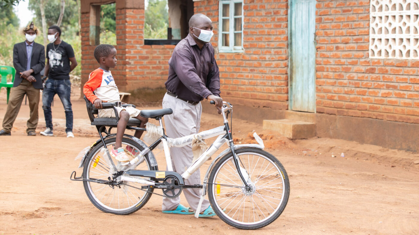 A man pushing an adapted bicycle with a child sitting on a seat at the back