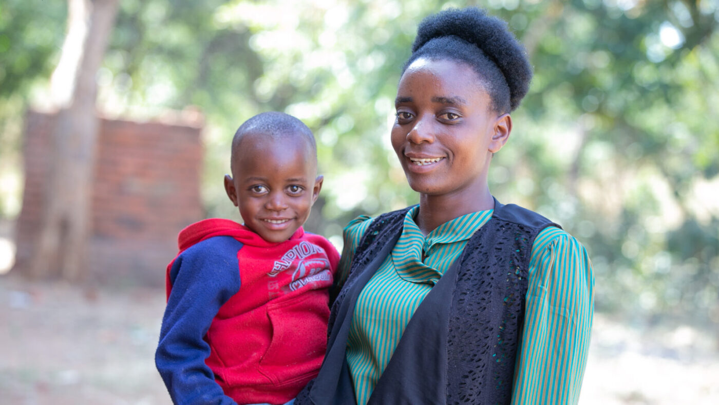 Catherine holds her son Wonderful as they stand outside smiling.