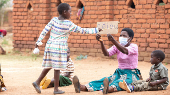 Girl pointing to the letter U at an outdoor school with other children