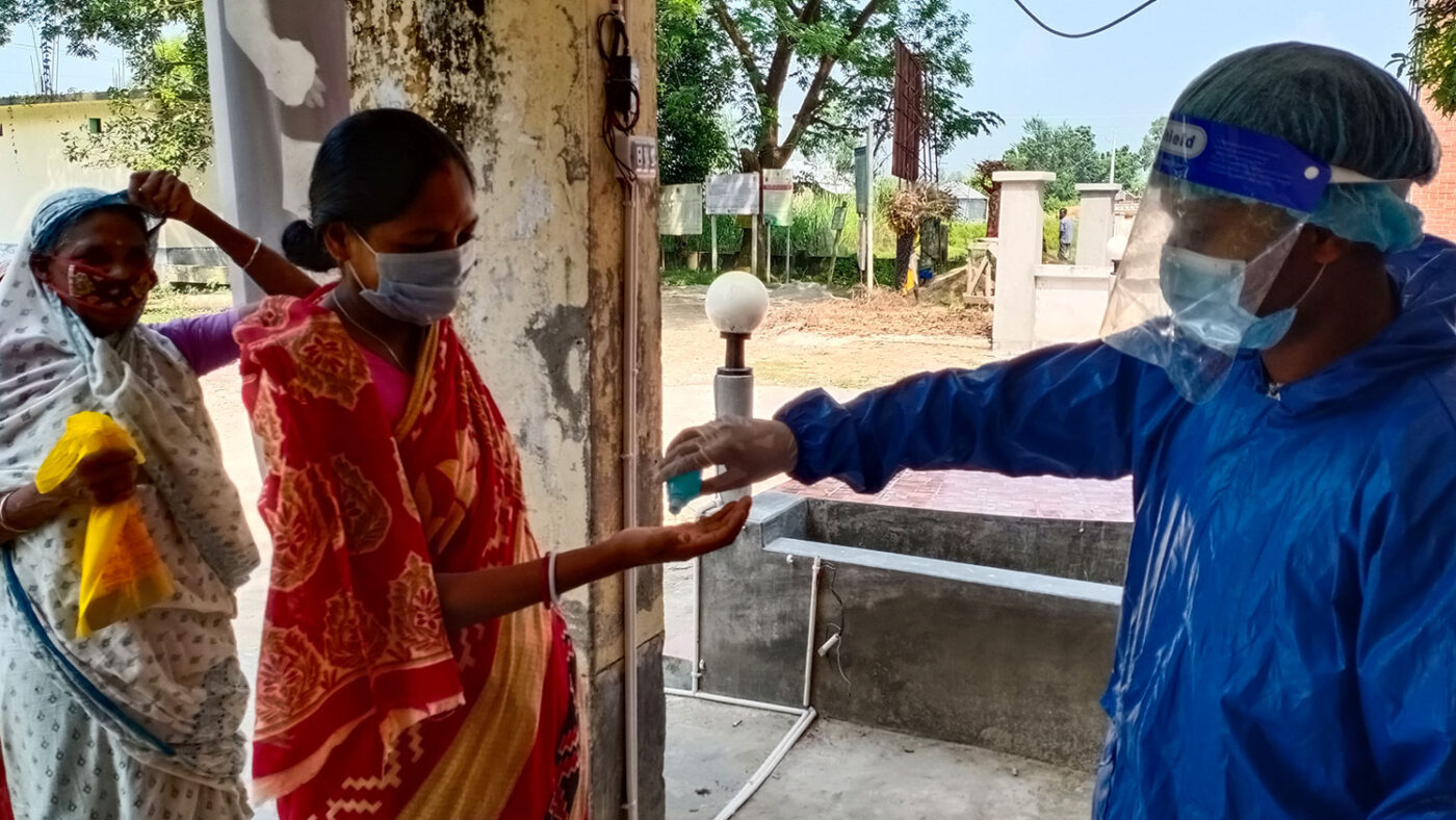 A woman holds her hand out while a health worker squirts hand sanitiser into it.