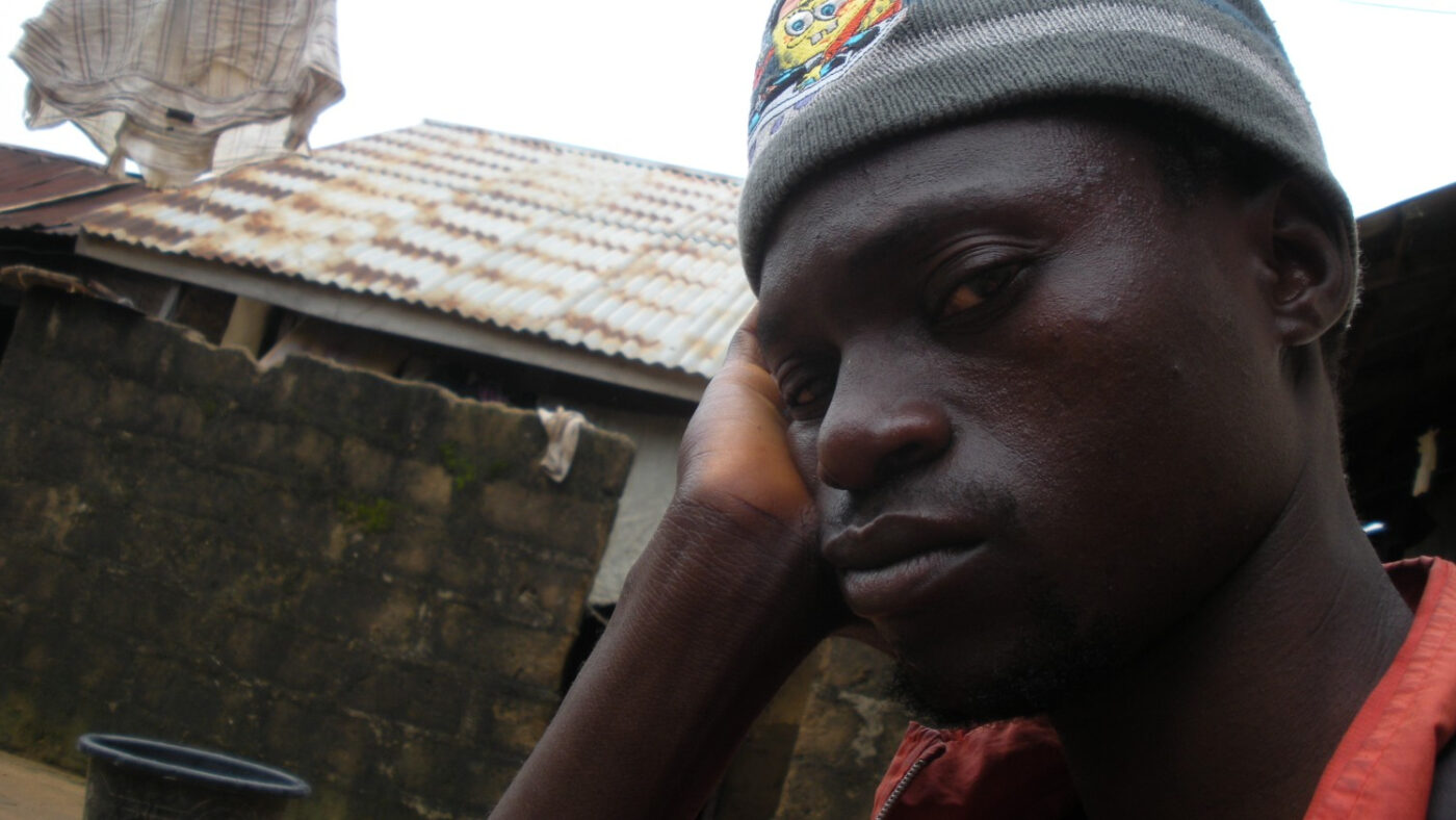 A man rests his head on his hand, and looks at the camera sadly.
