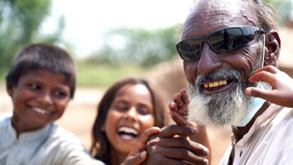 A man wearing sunglasses smiles with his two happy grandchildren.