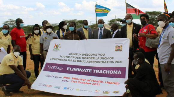 A large group of people hold a banner that celebrates the launch of the first cross-border mass drug administration for trachoma.