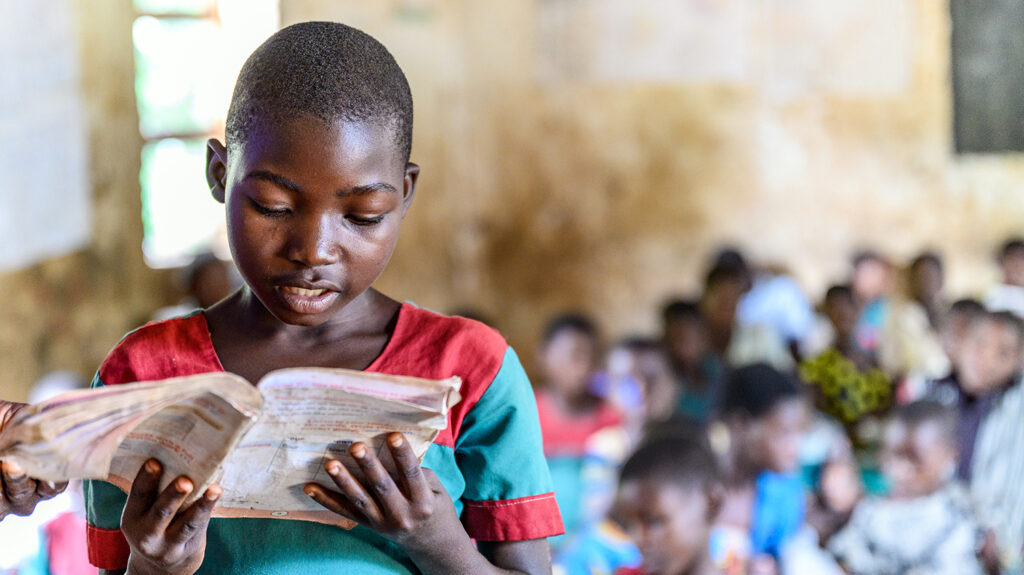 A girl reads a pamphlet with her classmates in the background.