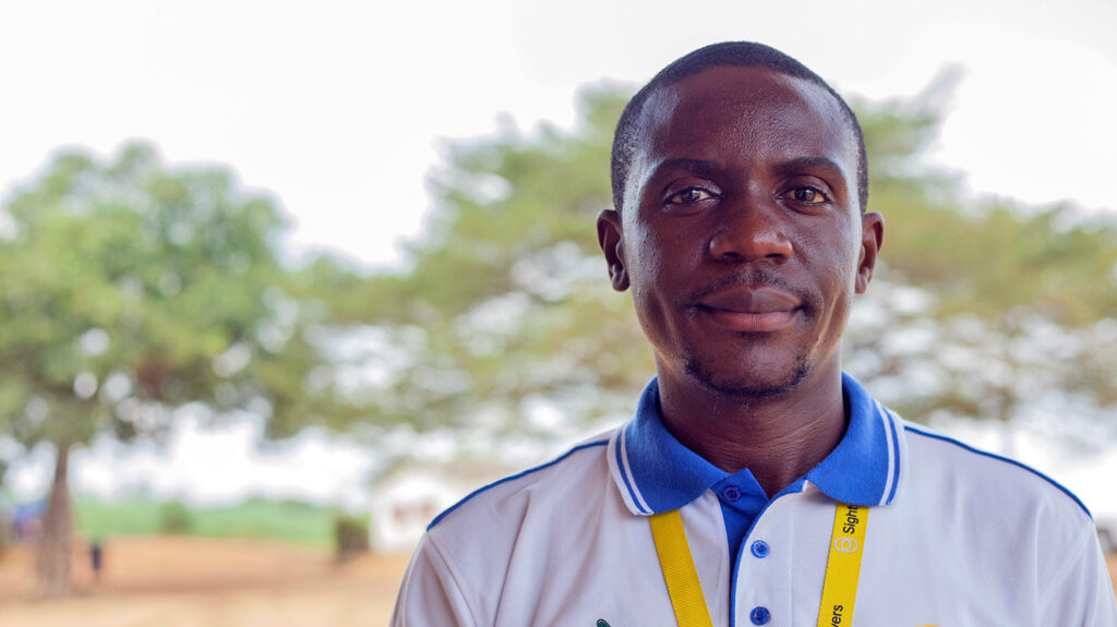 Mdelle Makoge wearing a Sightsavers lanyard, standing outside in Cameroon.
