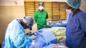 A surgical team carry out eye surgery while wearing bright blue and green surgical scrubs.