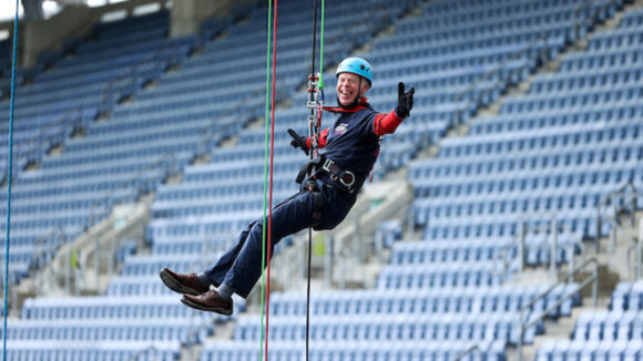 A man smiles and holds his arms out wide while abseiling.