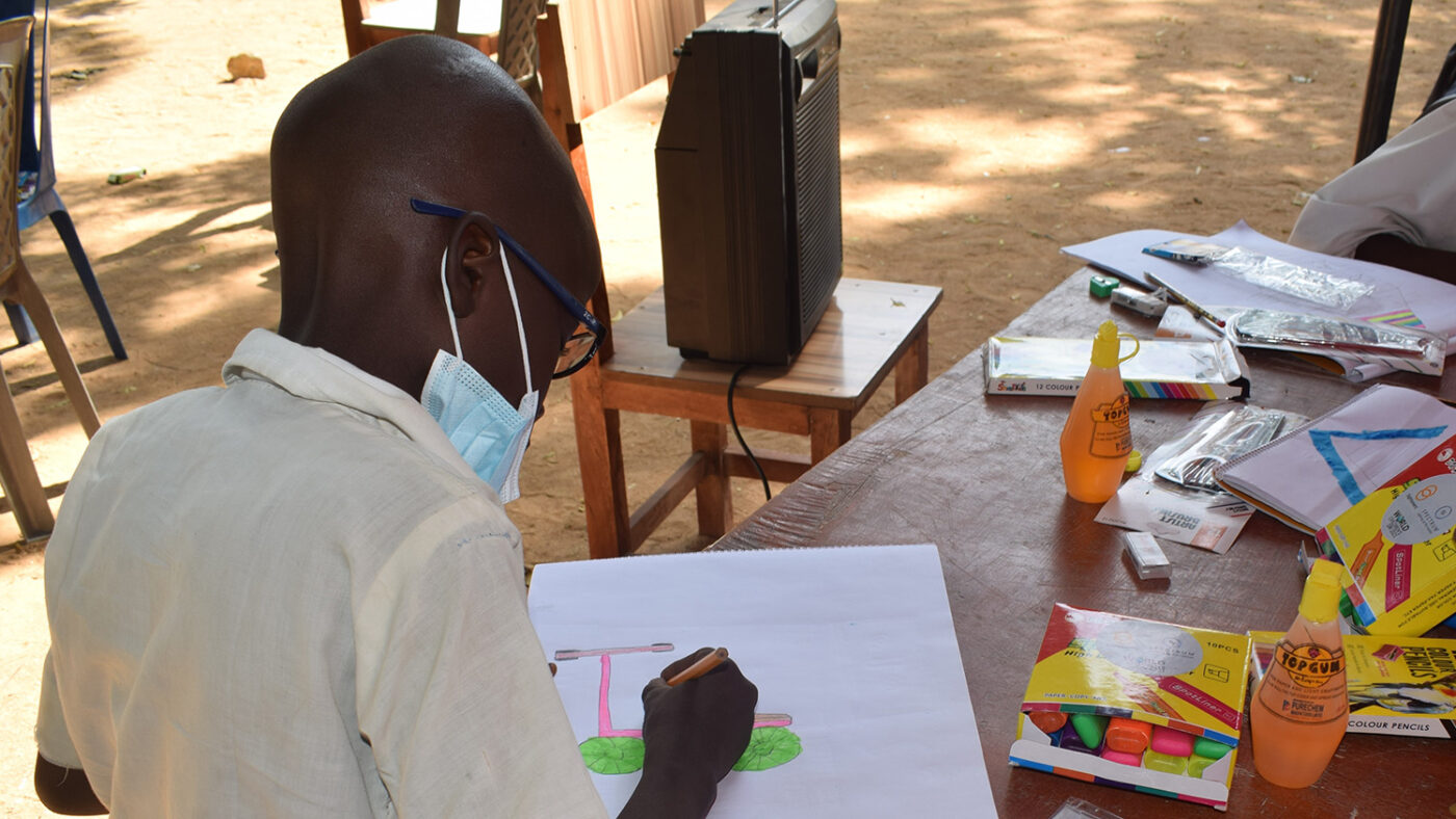 A young boy sitting at a table, drawing a bike with a colourful frame and wheels.