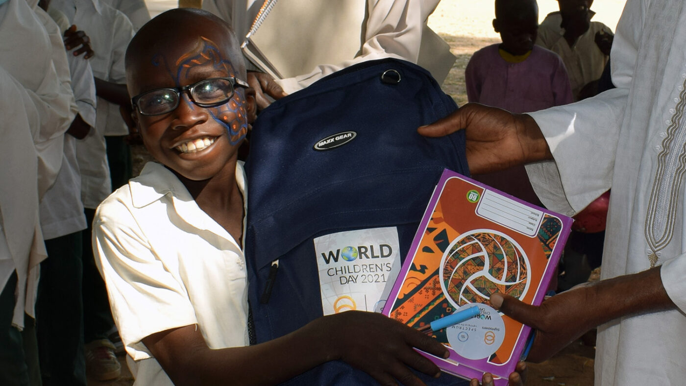 A smiling boy receives a gift of a backpack and art supplies.