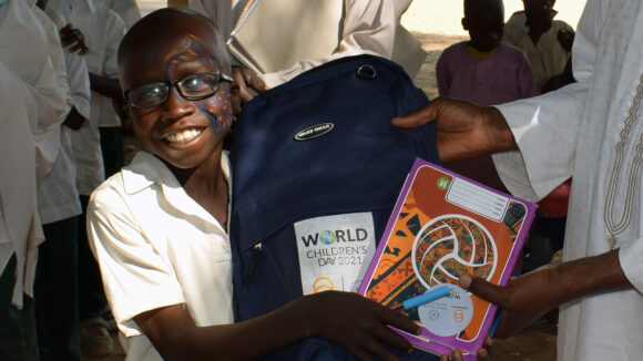 A smiling boy receives a gift of a backpack and art supplies.
