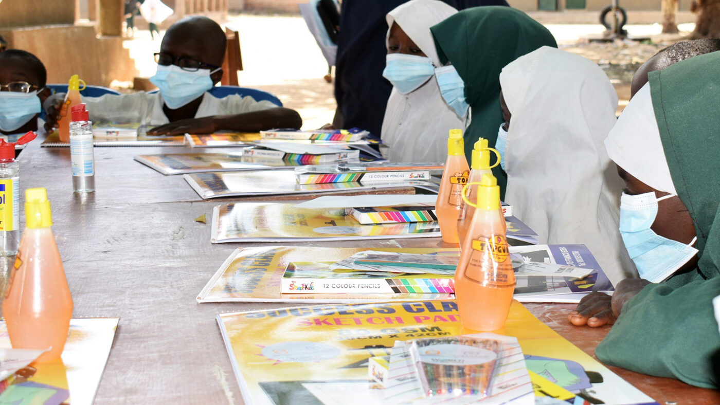 Children sit around a large table with art supplies in front of them.