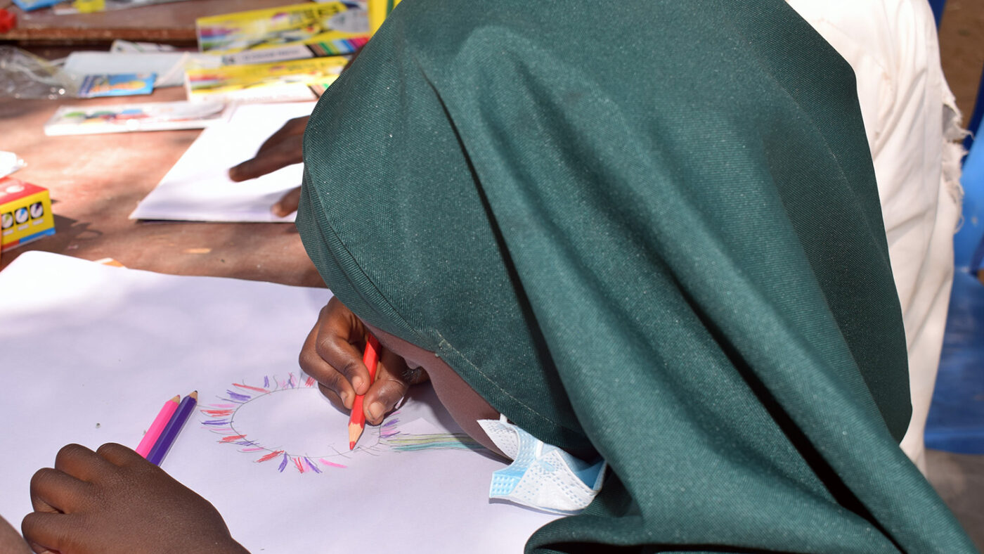 A girl sitting at a table drawing a picture of a flower.