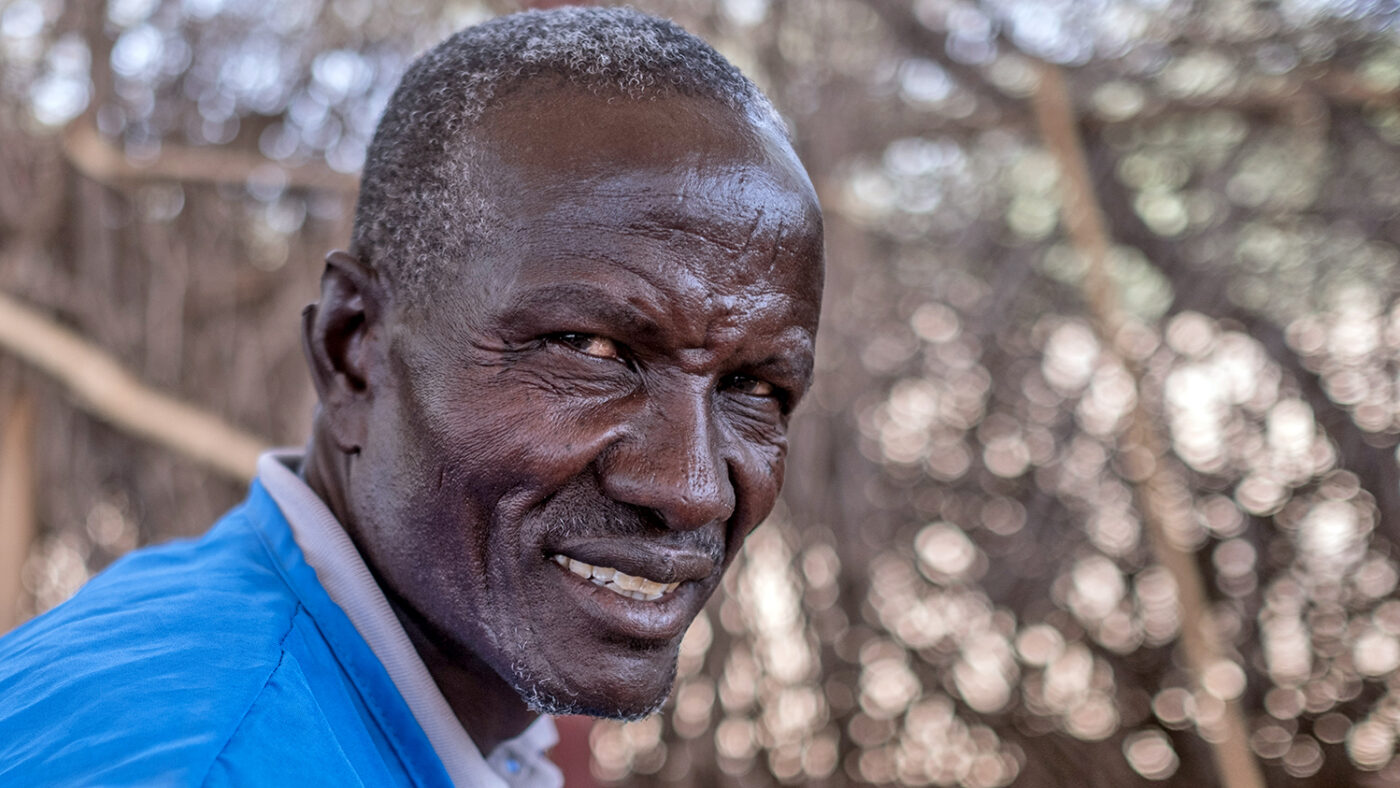 A man wearing a blue tabbard smiles at the camera.