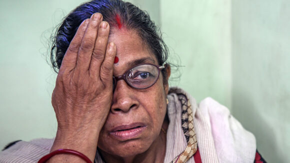 A woman wearing glasses holds one hand over her right eye during an eye test.