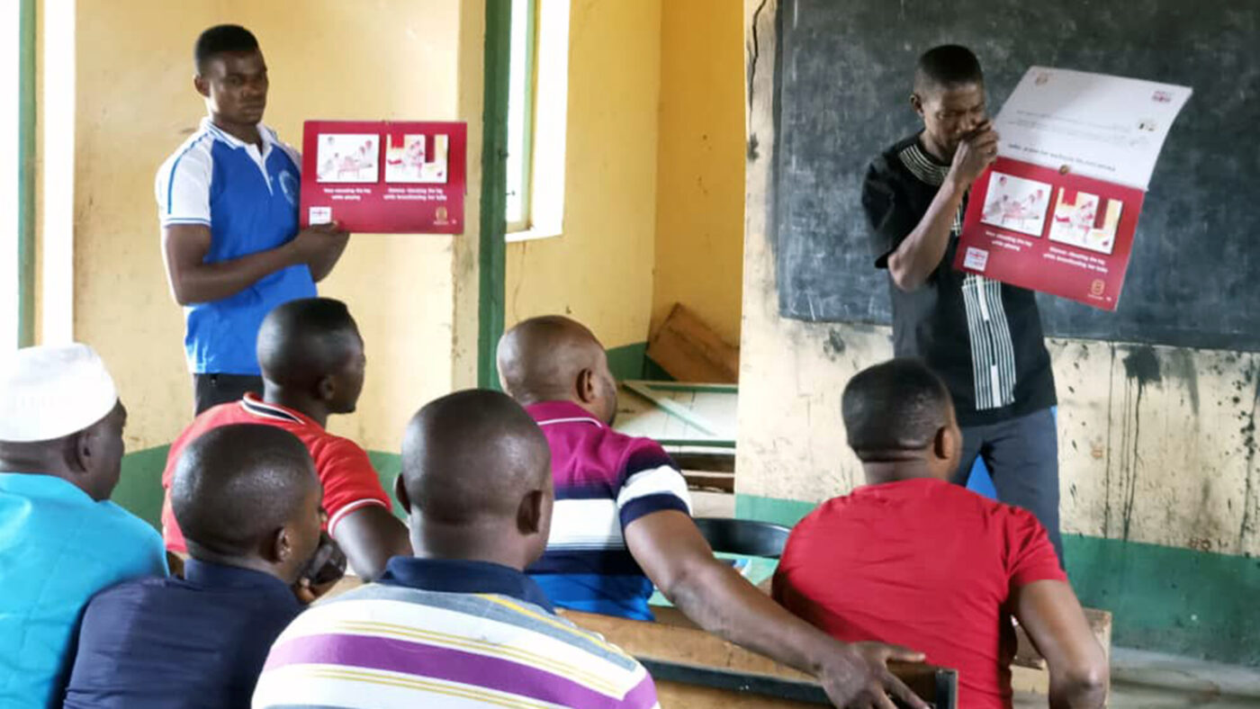 A group of volunteers sit in a room, with two trainers at the front holding up colourful cards.