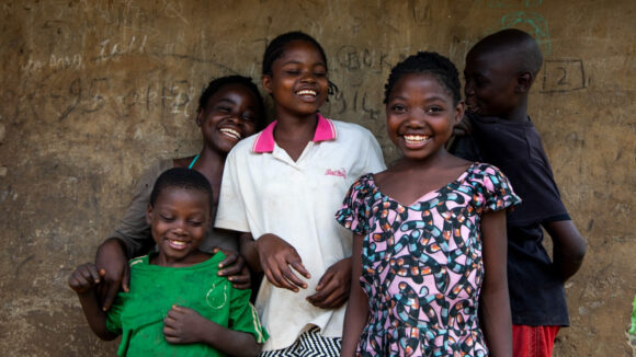 Nambo smiles with friends in front of their home.
