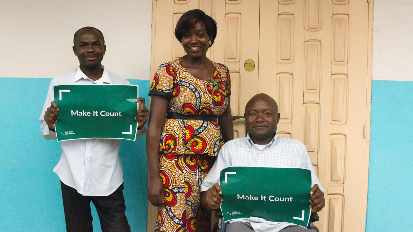 Two men and a woman in Cameroon. The men hold green posters saying 'Make it count'.
