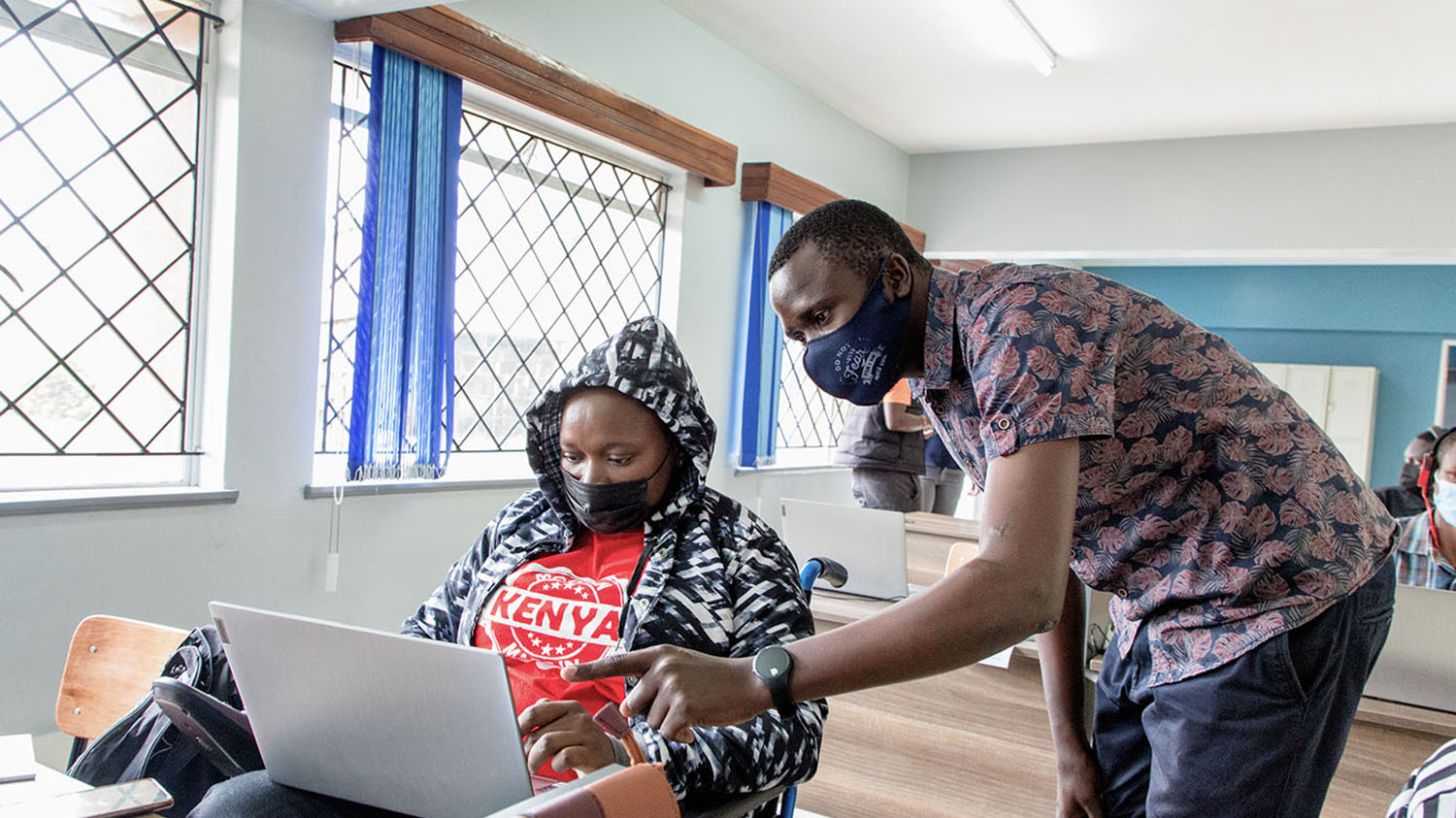 In a classroom, a student in a wheelchair receives tuition from a teacher.