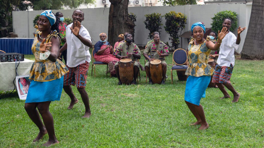 A group of men and women performing a traditional dance, accompanied by drummers.