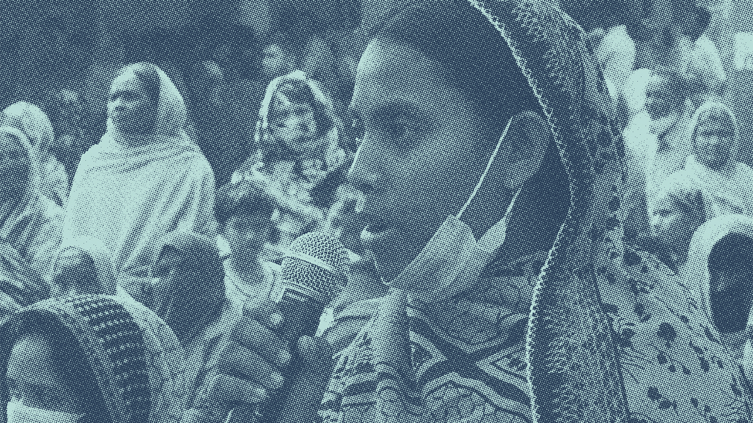 A woman wearing a mask on her chin speaks into a microphone. The image has a stylised blue tint.