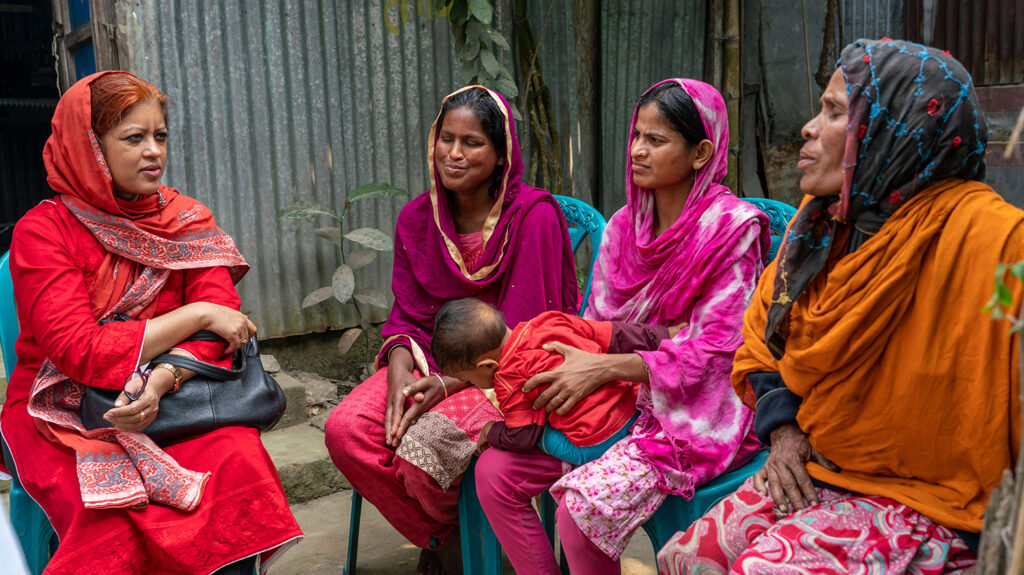Asma sits talking to three women, one of whom is holding a young child on her lap.