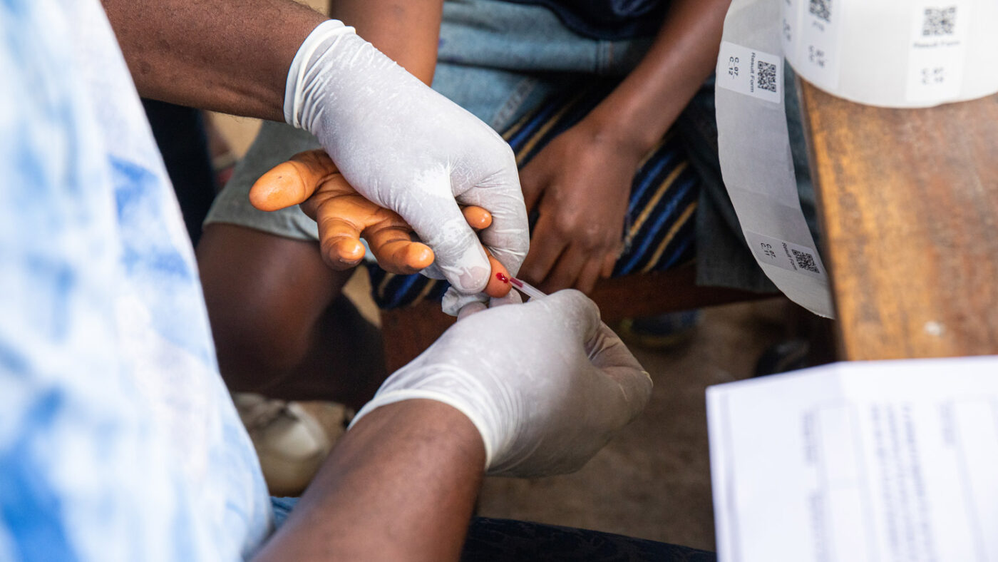 A health worker wearing surgical gloves takes a blood sample from a school student.