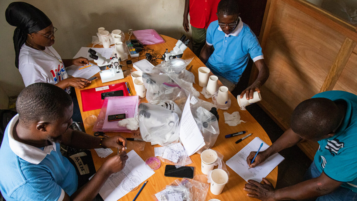 Four researchers work at a large table with samples and papers in front of them.
