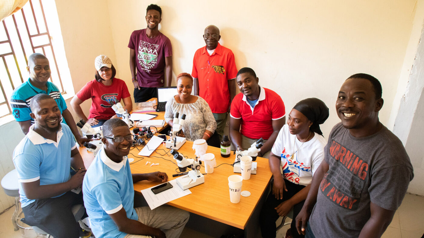 A group of male and female researchers gather around a table where there are papers and microscopes.