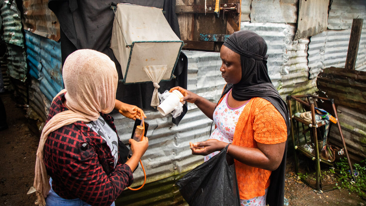 Two women stand outside a house to check a mosquito trap.