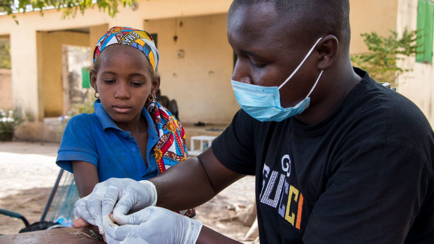 A health worker wearing a surgical mask takes a blood sample from a patient.