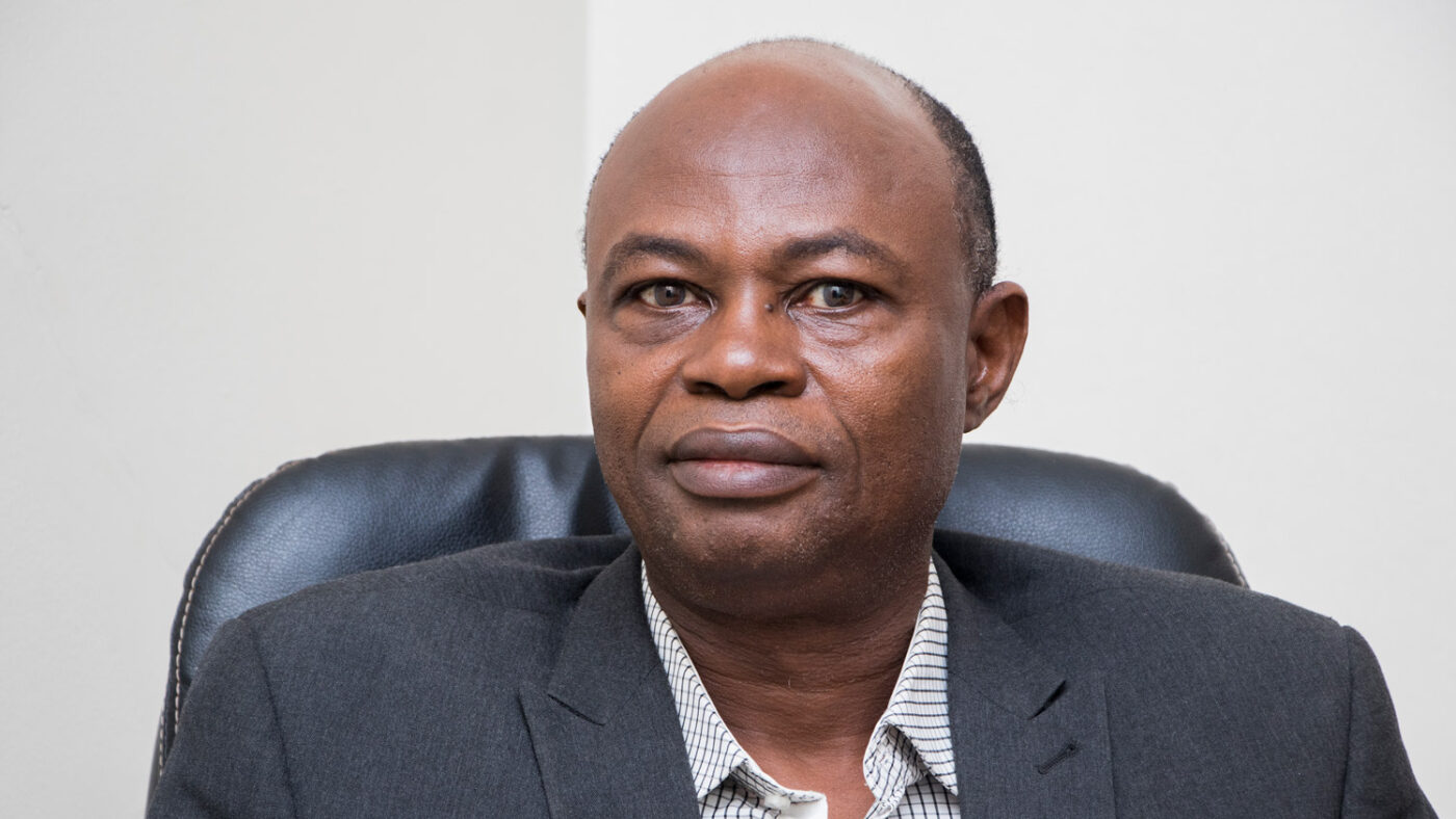 Elie Kamata sits in an office chair with a neutral expression on his face.